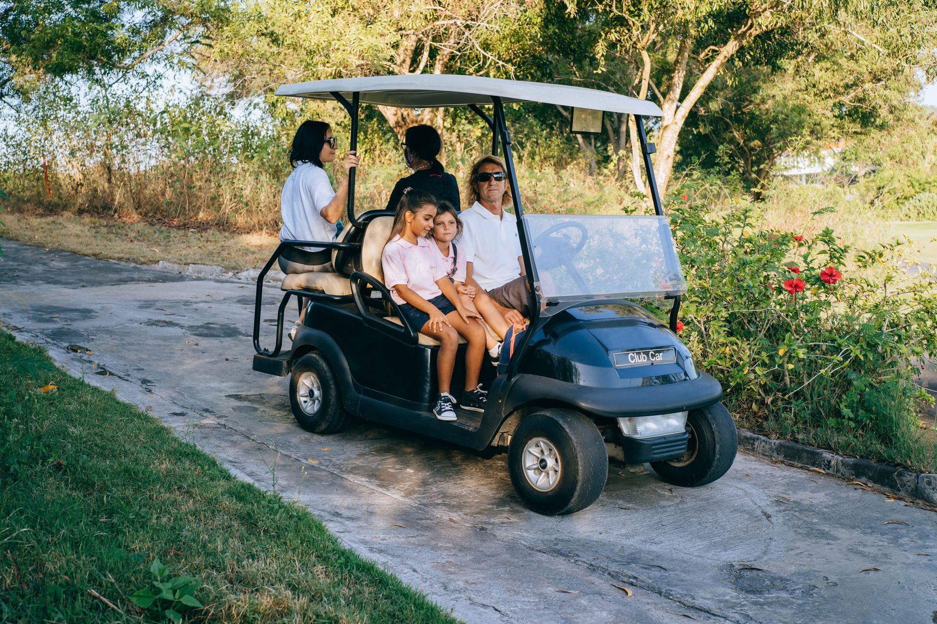 Family riding a golf cart down a palm-lined neighborhood path in warm afternoon light