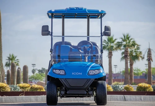 Straight-on front view of blue ICON i40 golf cart parked with palm trees in background