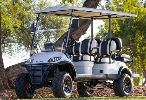 2025 ICON i60L lifted golf cart in white parked under trees — 6-passenger electric vehicle with off-road tires, deluxe seating, and tubular front bumper